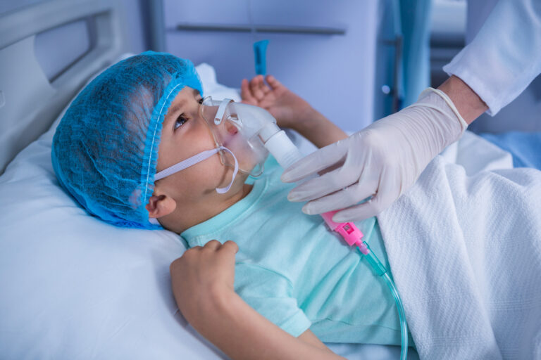 A doctor placing an oxygen mask on a young patient, representing KBB's children's surgery program